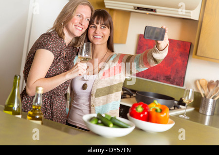 Metà femmina adulta amici prendendo autoritratto sullo smartphone in cucina Foto Stock