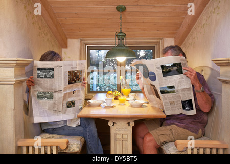 Coppia al tavolo per la colazione, ignorando ogni altro, leggendo i giornali Foto Stock