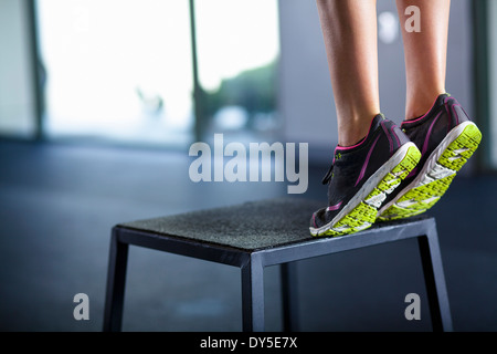 Giovane donna tiptoeing sul bordo di uno sgabello Foto Stock