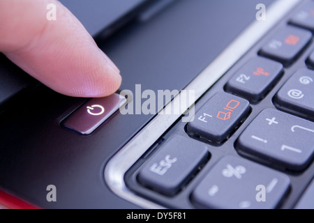 Un dito è premendo il pulsante di accensione per riattivare il computer portatile fino Foto Stock