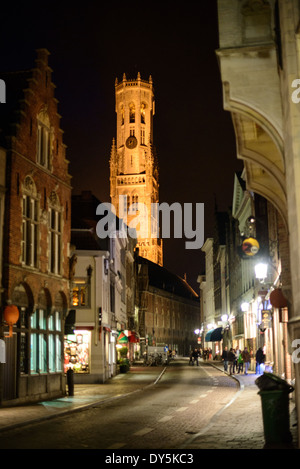 Belfry Tower Night View Bruges Belgio // BRUGES, Belgio — Vista notturna di una strada storica nel centro medievale di Bruges, con la torre Belfry illuminata che sorge sullo sfondo. Il Belfry, un campanile medievale completato nel XV secolo, si erge come uno dei punti di riferimento più importanti della città sulla piazza Markt. La struttura, alta 83 metri (272 piedi), Patrimonio dell'Umanità dell'UNESCO, è un simbolo iconico della prosperità medievale e del patrimonio architettonico di Bruges. Foto Stock