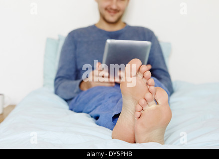 Metà uomo adulto giacente sul letto tramite tavoletta digitale Foto Stock