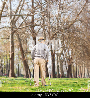 Senior uomo a camminare con le stampelle nel parco, vista posteriore Foto Stock