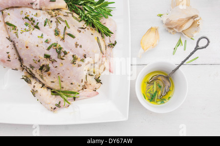 Il pollo intero con olio, rosmarino e aglio, preparazione per grill la tostatura su bianco tavolo in legno Foto Stock