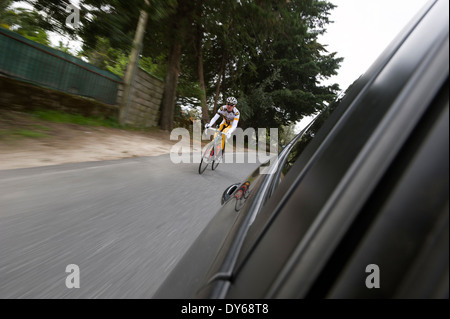 Ciclista professionista racing con una strada in discesa visto dall'interno di un automobile Foto Stock