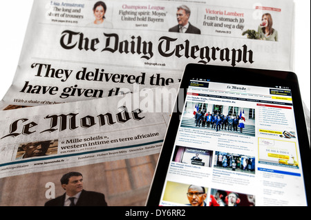 Tablet con online notizie internazionali sulla sommità del britannico Daily Telegraph e il francese Le Monde quotidiani su sfondo bianco Foto Stock