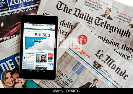 Tablet che mostra online news del Huffington Post sulla sommità del britannico Daily Telegraph e il francese Le Monde quotidiani europei Foto Stock