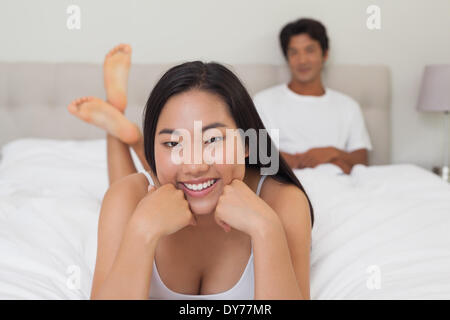 Donna sdraiata sul letto sorridente in telecamera Foto Stock