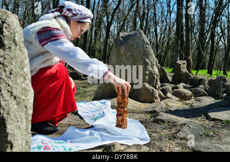 "Pagane" di Pasqua in Ucraina. Preparazione per la celebrazione di Pasqua: donna in abiti tradizionali imposta l'idolo di legno. Foto Stock