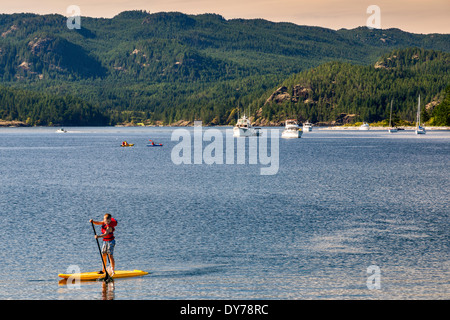 Giovane ragazzo in piedi, paddleboarding, Rebecca Spit provinciale parco marino, Quadra Island, British Columbia, Canada Foto Stock