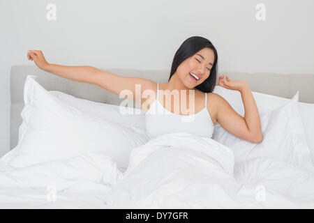 Donna sorridente giacente in letto stretching al mattino Foto Stock