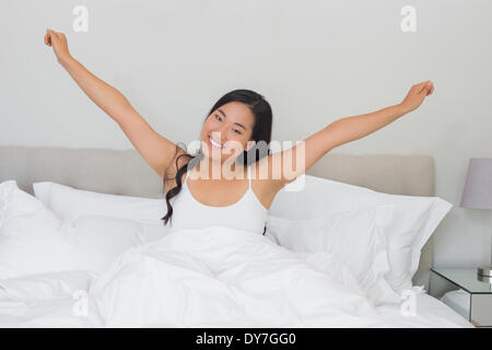 Donna sorridente stretching nel letto la mattina Foto Stock