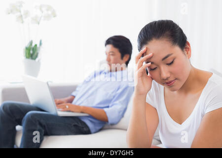 Sconvolto donna seduta sul divano mentre fidanzato utilizza laptop Foto Stock