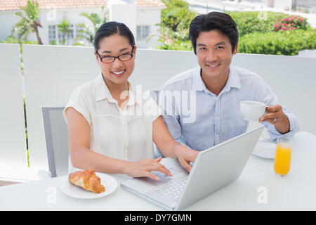 Coppia sorridente avente la colazione insieme utilizzando il computer portatile Foto Stock