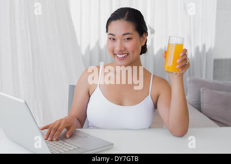 Donna felice utilizzando laptop e di succo di arancia Foto Stock