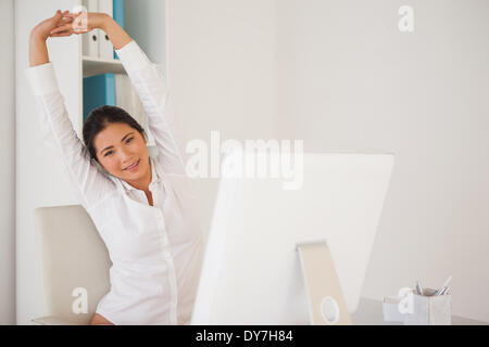 Casual imprenditrice stretching alla sua scrivania Foto Stock