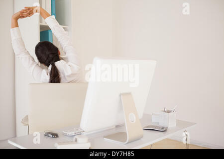 Casual imprenditrice stretching alla sua scrivania Foto Stock