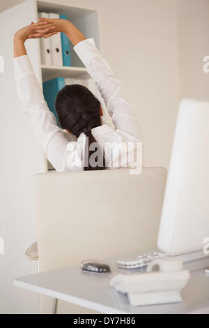 Casual imprenditrice stretching alla sua scrivania Foto Stock