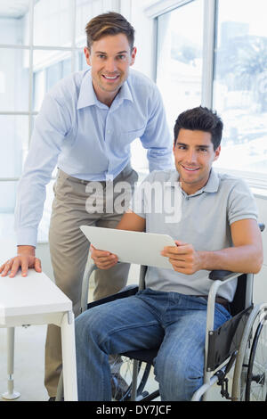 Imprenditore casual in carrozzella sorridente in telecamera con un collega Foto Stock