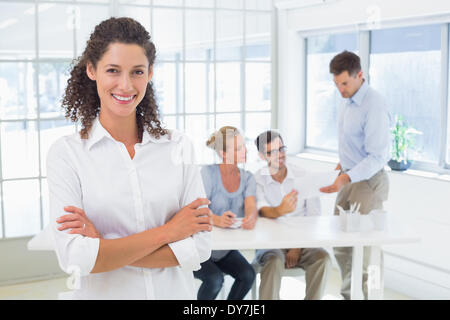 Casual imprenditrice sorridente in telecamera con il team dietro di lei Foto Stock