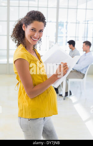 Casual incinta imprenditrice la scrittura nella cartella sorridente in telecamera Foto Stock