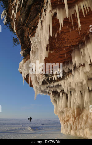 Ghiaccioli appesi da pietra arenaria rossa cliff e la gente che camminava sul lago ghiacciato di Superior, Apostle Islands National Lakeshore Foto Stock