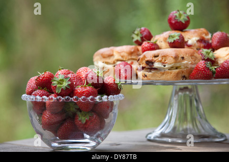 Le fragole in un recipiente di vetro, scones con panna e marmellata su una torta di stand Foto Stock