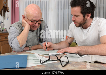 Nipote aiutando il suo nonno facendo dichiarazione fiscale Foto Stock