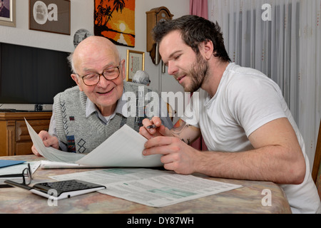 Nipote aiutando il suo nonno facendo dichiarazione fiscale Foto Stock