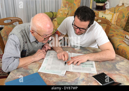 Nipote aiutando il suo nonno facendo dichiarazione fiscale Foto Stock