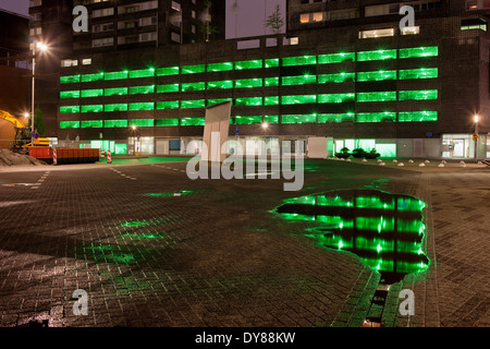 Urban astratta, luci verdi di un multipiano parcheggio con riflessi sull'acqua dopo la pioggia durante la notte . Foto Stock