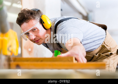 Carpenter lavorando su un ronzio elettrico visto il taglio di alcune schede, indossa gli occhiali di sicurezza e la protezione dell'udito Foto Stock