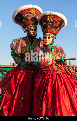 Due donne nel bellissimo centro storico rosso fancy dress costume, maschere e cappelli che pongono sotto il sole, il Carnevale di Venezia, il Carnevale di Venezia, Italia Foto Stock