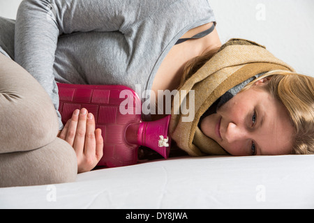 Giovane donna nel dolore, allevia il dolore associato con bottiglie di acqua calda Foto Stock