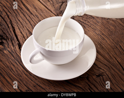 Versare il latte dalla bottiglia nella tazza bianca. Foto Stock