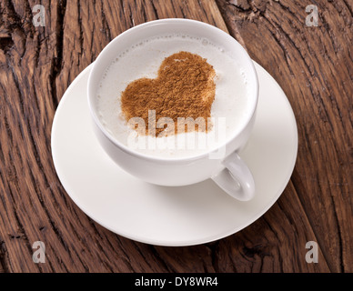 Tazza di cappuccino con cannella in polvere in forma di cuore sul vecchio tavolo in legno. Vista dall'alto. Foto Stock