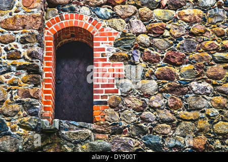 Il vecchio sportello in acciaio incorniciato mattoni rossi nel muro di pietra Foto Stock