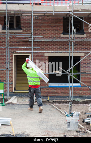 Il lavoro di un uomo che porta una nuova finestra in PVC per essere installato in una nuova casa in costruzione Foto Stock
