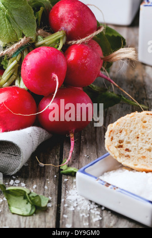 Fresche ravanelli bagnato con sale marino e pane su un vecchio tavolo in legno Foto Stock