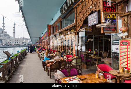 Ristoranti di pesce sotto il ponte Galata attraverso Golden Horn con nuova moschea (Yeni Camii) dietro, quartiere Eminonu, Istanbul, Turchia Foto Stock