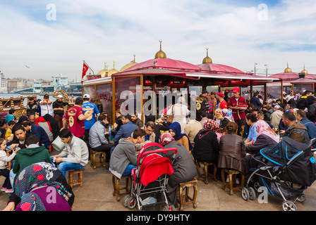 La gente del posto e turisti di mangiare da imbarcazioni di vendita del pesce panini vicino al Ponte di Galata, quartiere Eminonu, Istanbul, Turchia Foto Stock