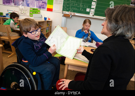 Non-disabili e gli studenti disabili (in questo caso un ragazzo su una sedia a rotelle) imparare insieme nella stessa classe in una scuola primaria. Foto Stock