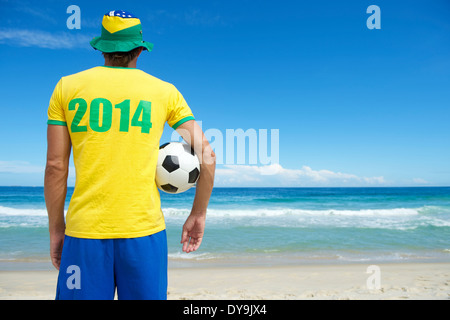 Il brasiliano giocatore di calcio in Brasile colori 2014 shirt e hat holding calcio spiaggia tropicale Foto Stock