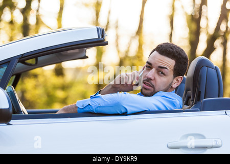 Giovani Latinoamericani conducente facendo una telefonata durante la guida Foto Stock