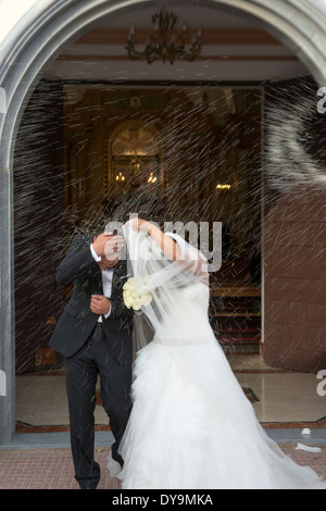 La sposa e lo sposo ricevere riso gettando familiari al di fuori della chiesa e gli amici sui loro giorno di nozze Foto Stock