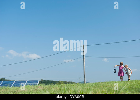 I bambini a camminare in campo nei pressi di pannelli solari e linee di alimentazione, che porta vecchia lanterna Foto Stock
