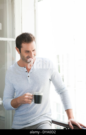 Uomo in piedi dalla finestra con la tazza in mano Foto Stock
