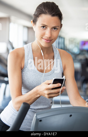 Giovane donna se si ascolta musica mentre si utilizzano passo scalatore in palestra Foto Stock