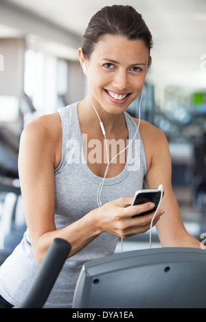 Giovane donna se si ascolta musica mentre si utilizzano passo scalatore in palestra Foto Stock