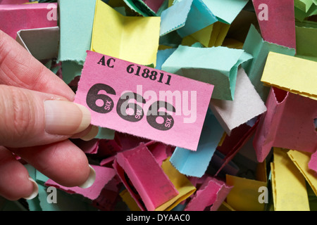 pile di biglietti per lotterie di diversi colori con selezione a mano biglietto rosa vincente numero 666 Foto Stock